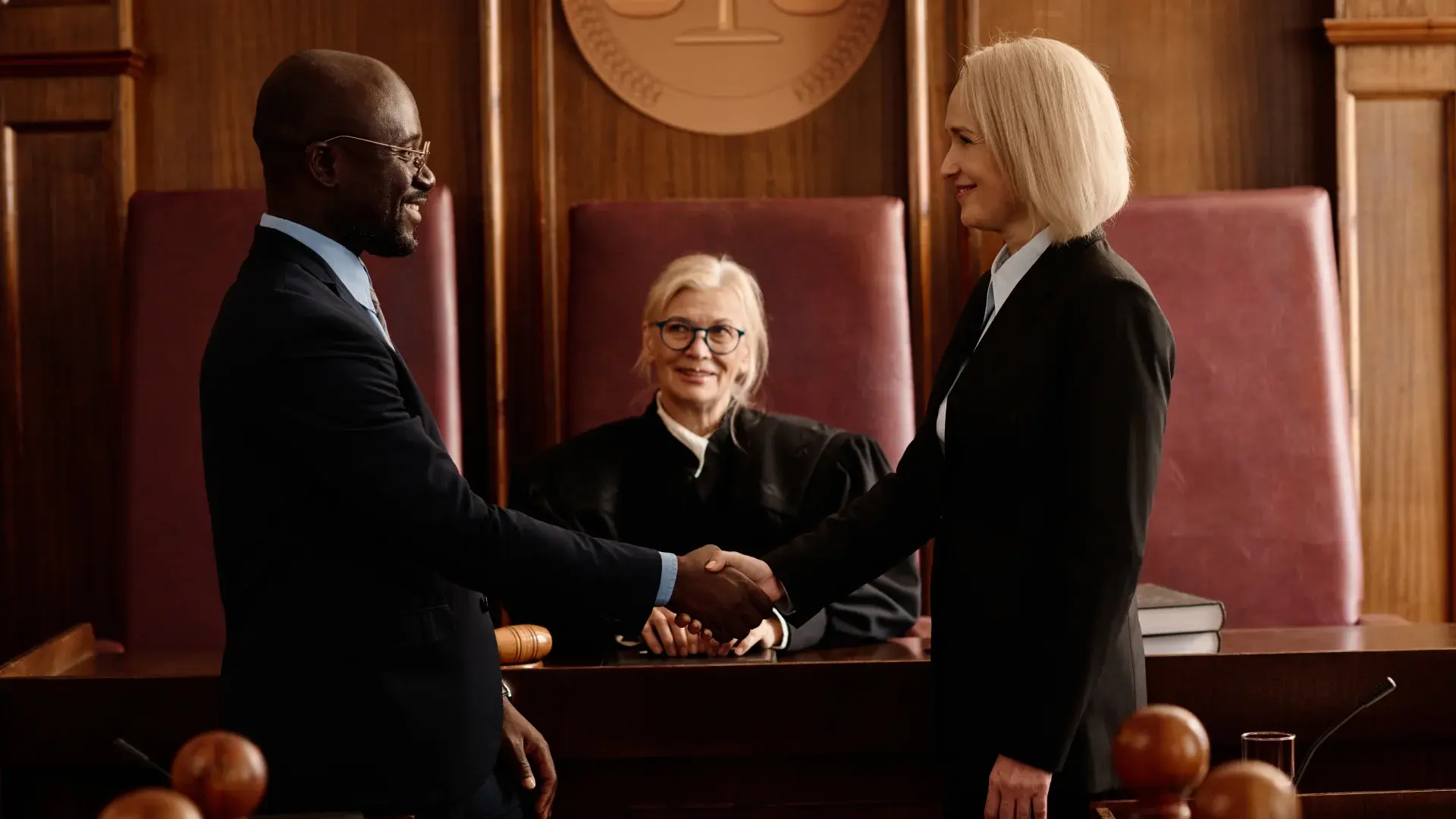 Two lawyers shaking hands in a courtroom while a judge looks on